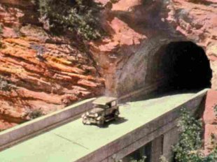 This 1930s-era hand-colored photograph shows the east side of Zion Tunnel, where a bridge was built to span a steep and narrow canyon. Credit: National Park Service